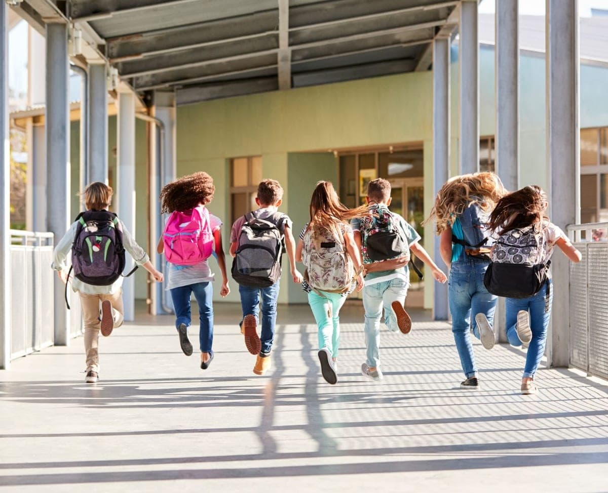 Children with backpacks running along a covered school walkway